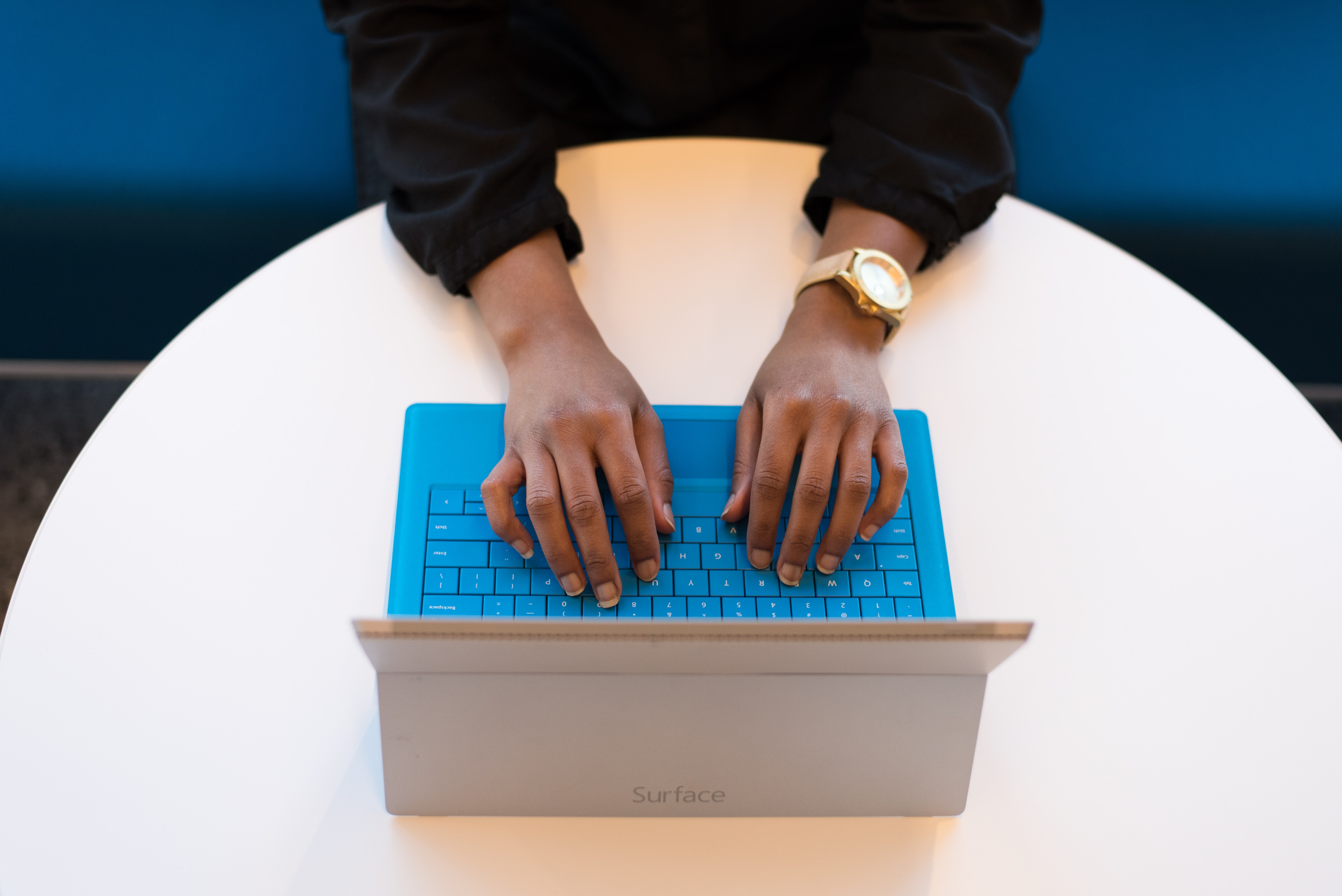 hands of woman with gold watch typing on blue laptop